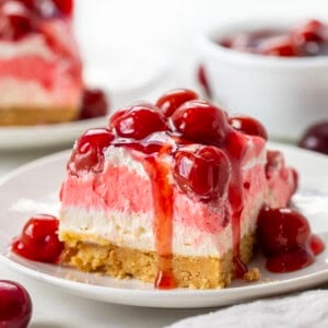 Piece of Cherry Delight on a white plate with cherries dripping off edge.