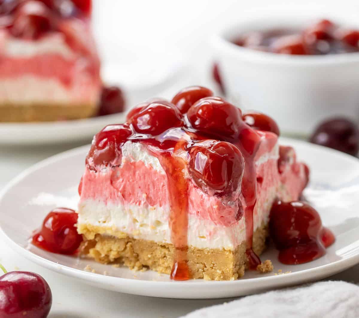 Piece of Cherry Delight on a white plate with cherries dripping off edge.