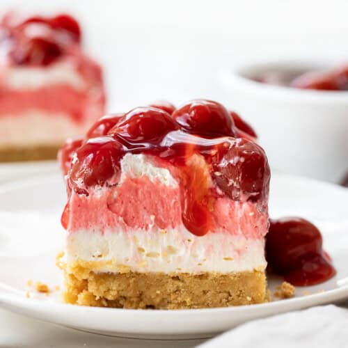 Piece of Cherry Delight on a white plate with cherries dripping off edge.