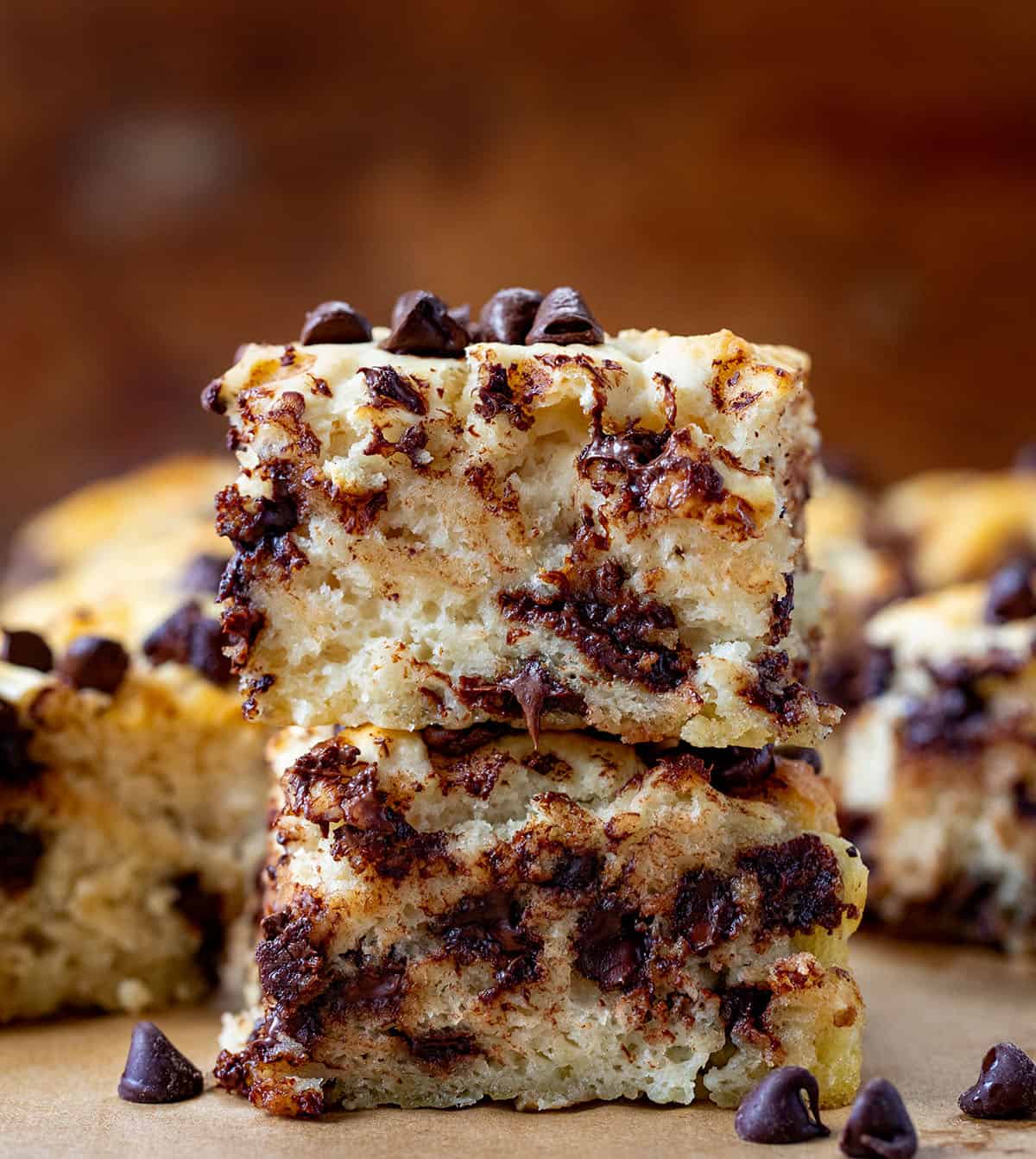 Stack of mile-high Chocolate Chip Butter Swim Biscuits on a wooden table surrounded by more biscuits and chocolate chips.