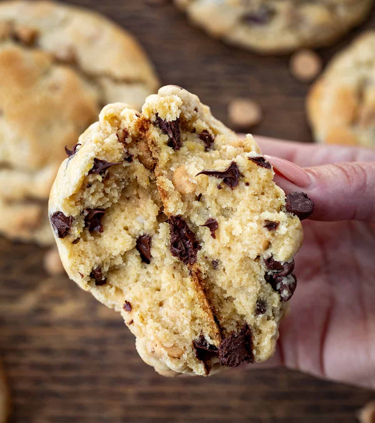 Hand holding a Thick and Chewy Peanut Butter Chocolate Chip Cookies that has been halved.