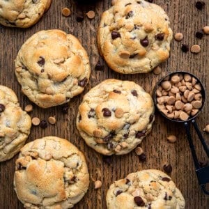 Thick and Chewy Peanut Butter Chocolate Chip Cookies on a cutting board with chocolate chips and peanut butter chips.