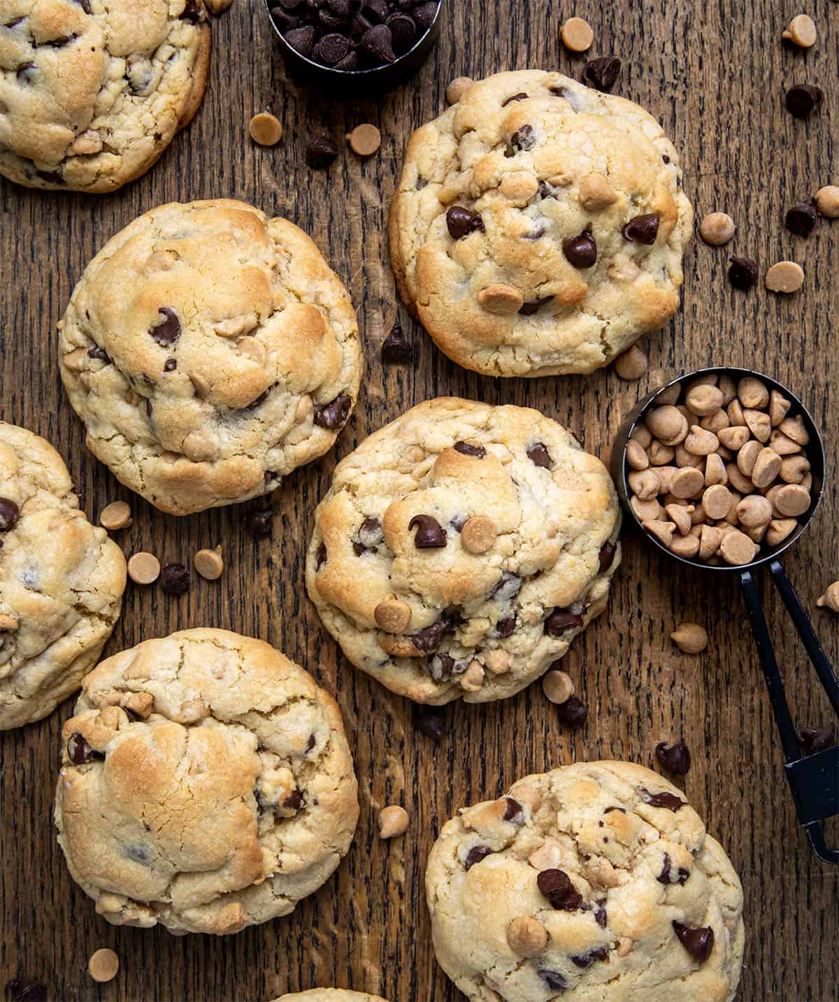 Thick and Chewy Peanut Butter Chocolate Chip Cookies on a cutting board with chocolate chips and peanut butter chips.