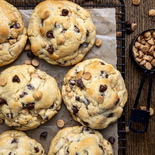 Thick and Chewy Peanut Butter Chocolate Chip Cookies on a cutting board with chocolate chips and peanut butter chips.