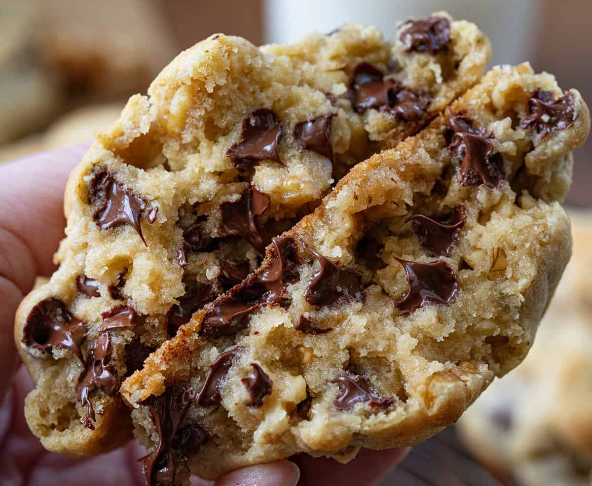 Hand holding a broken in half Copycat Levain Bakery Chocolate Chip Cookie or a chocolate chip walnut cookie.