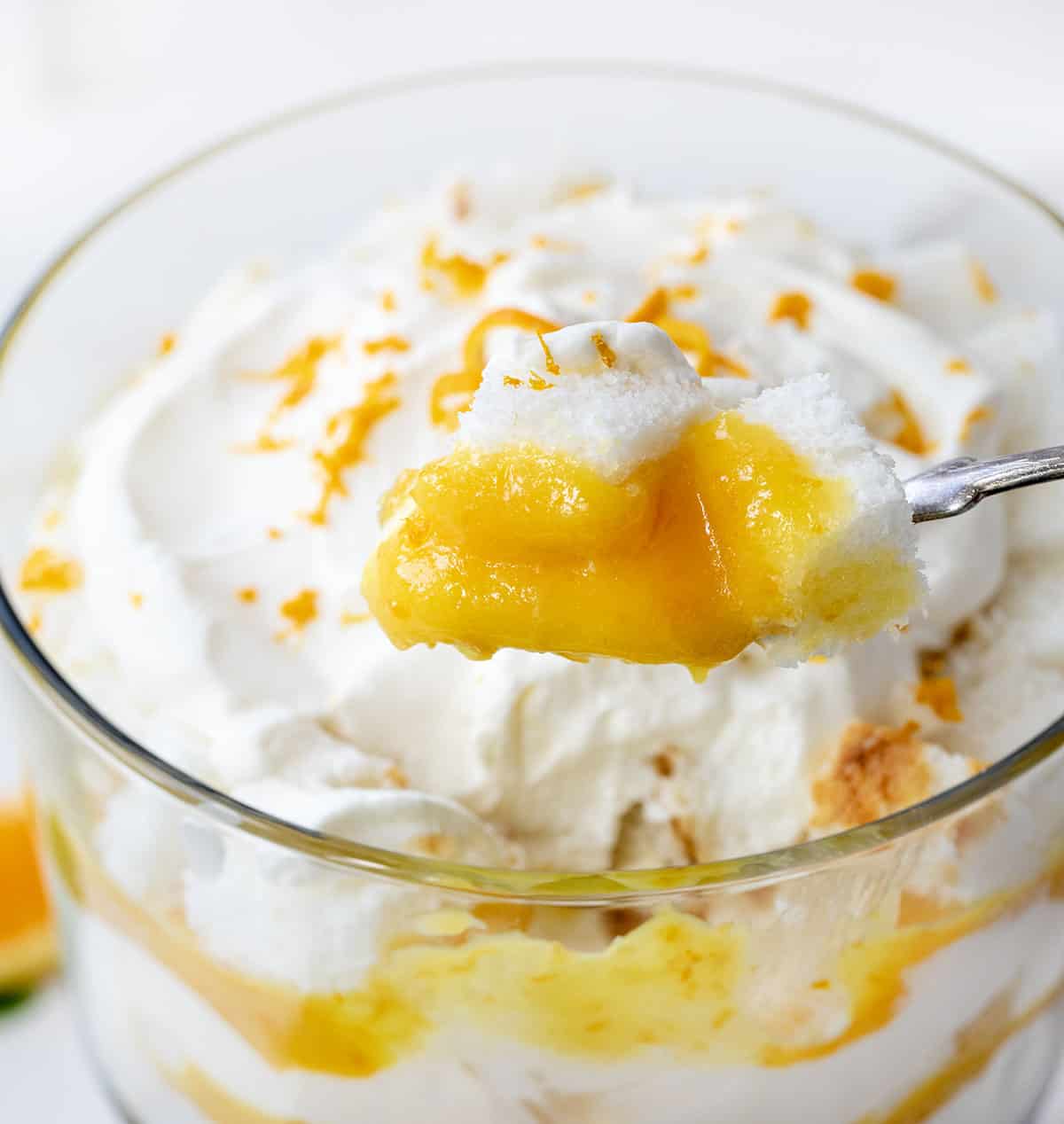 Taking a scoop of Creamsicle Trifle on a white counter surrounded by oranges and mint.