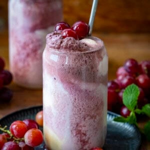 A couple of Dirty Grape Floats on a wooden table with fresh grapes around.