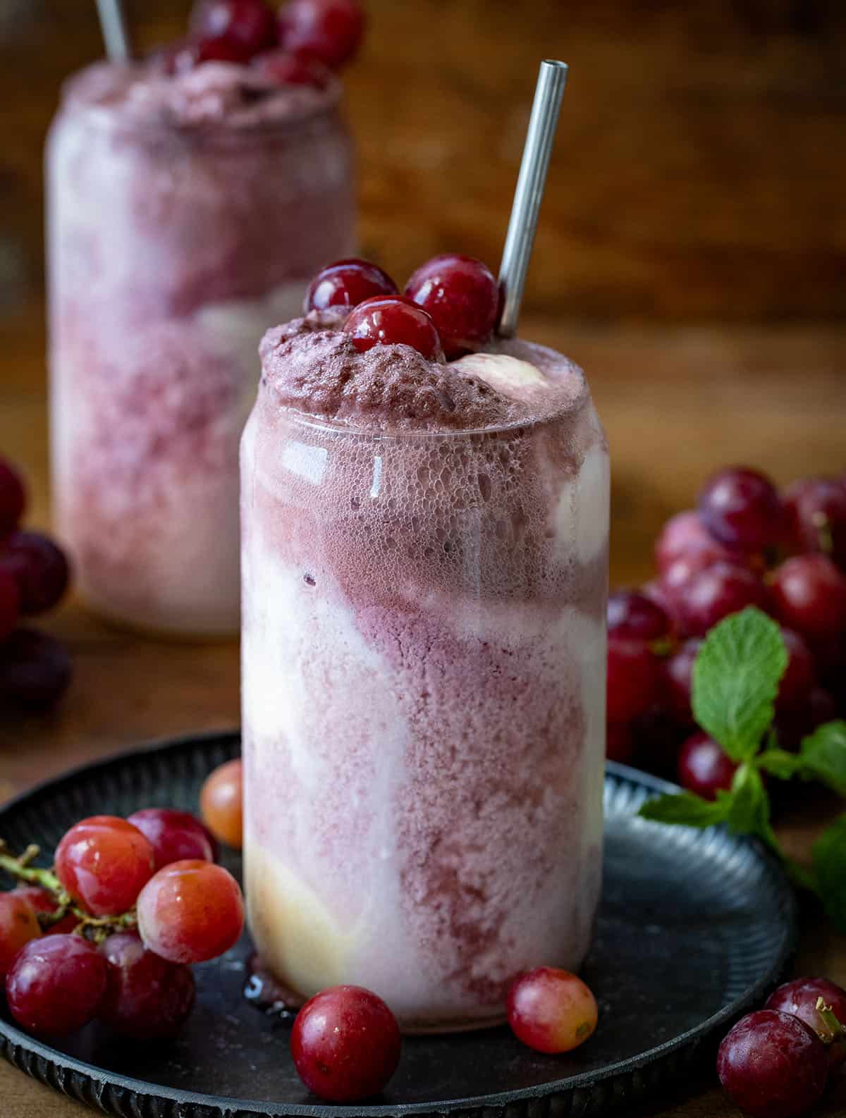 A couple of Dirty Grape Floats on a wooden table with fresh grapes around. 