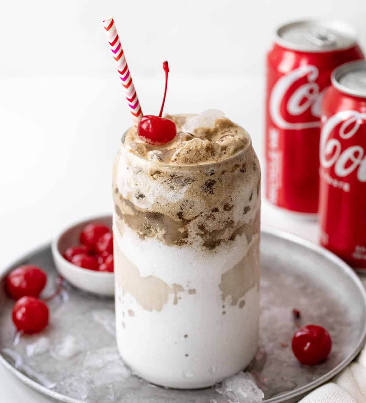 Glass of Fluffy Coke on a tray with ice and cherries.