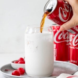 Pouring Coke into a glass that is coated with marshmallow fluff.