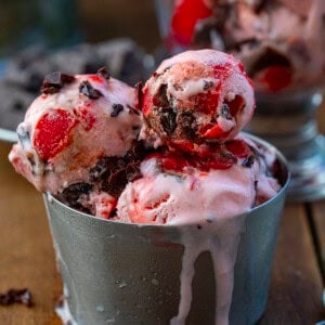 Cup of Chocolate Cherry Ice Cream that is melting on a wooden table.