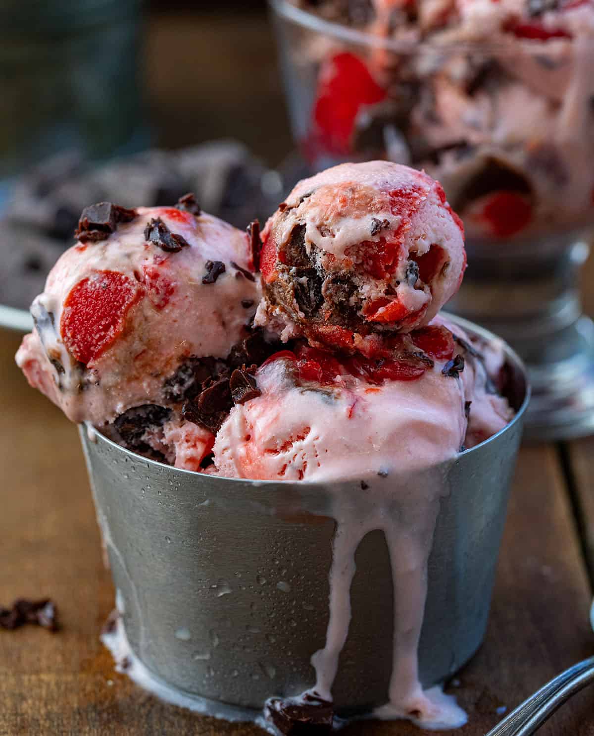 Cup of Chocolate Cherry Ice Cream that is melting on a wooden table.