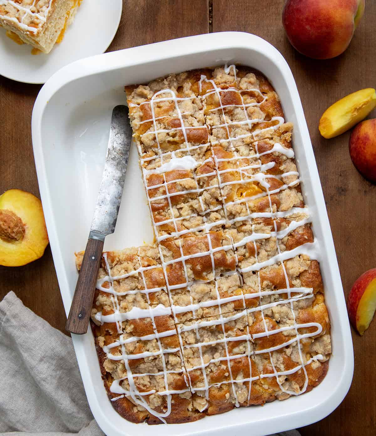 Pan of Peach Crumb Cake on a wooden table with a couple of pieces removed and plated from overhead.