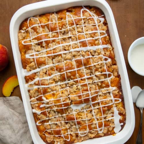 Pan of Peach Crumb Cake on a wooden table with fresh peaches from overhead.