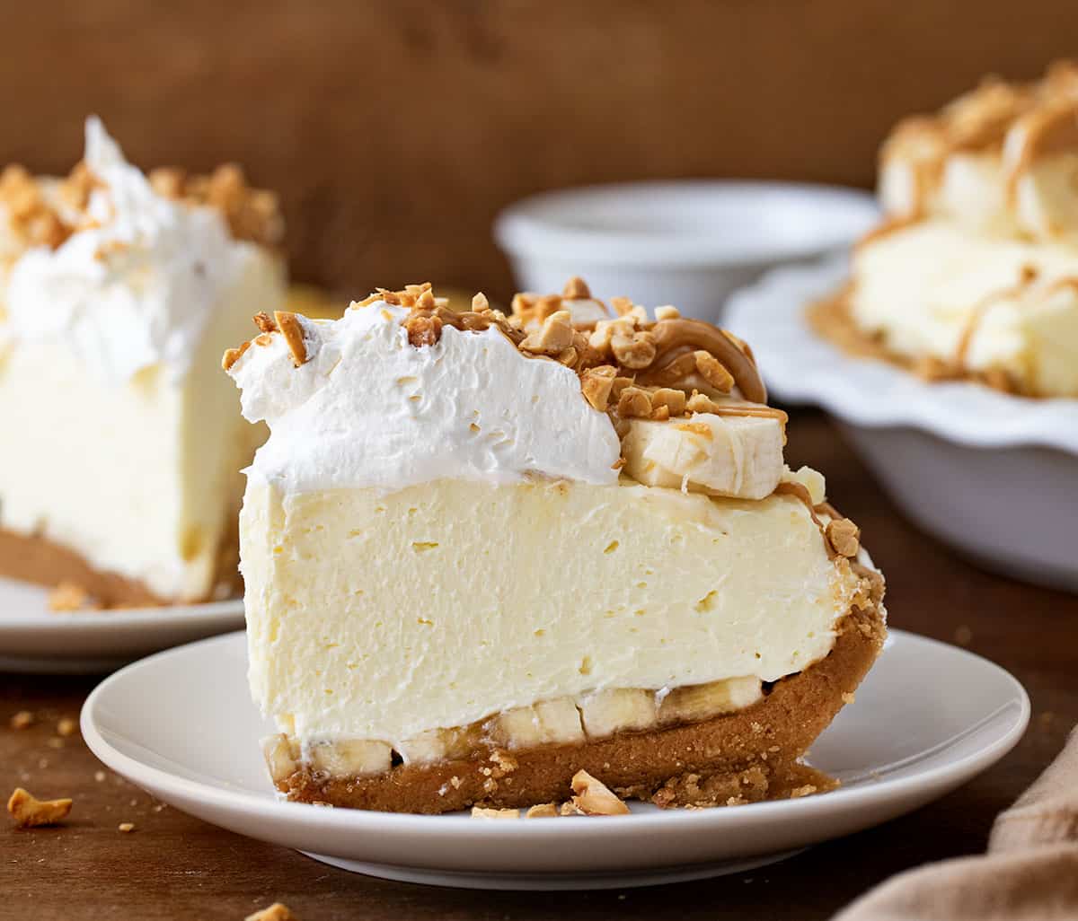 Slice of Peanut Butter Banana Cream Pie on a white plate on a wooden table.