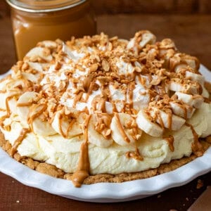 Peanut Butter Banana Cream Pie on a wooden table in a white cake plate.