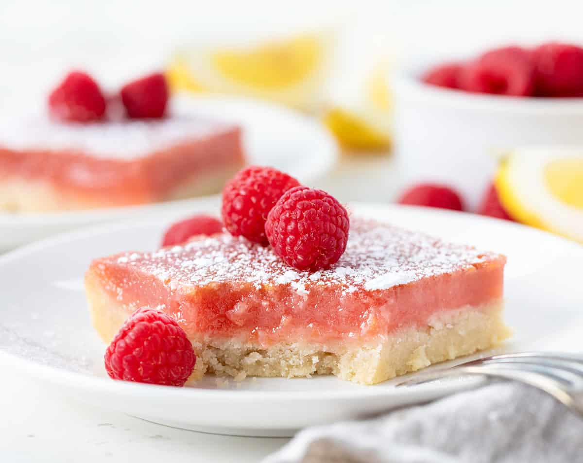 Raspberry Lemon Bar on a white plate with a bite taken out.