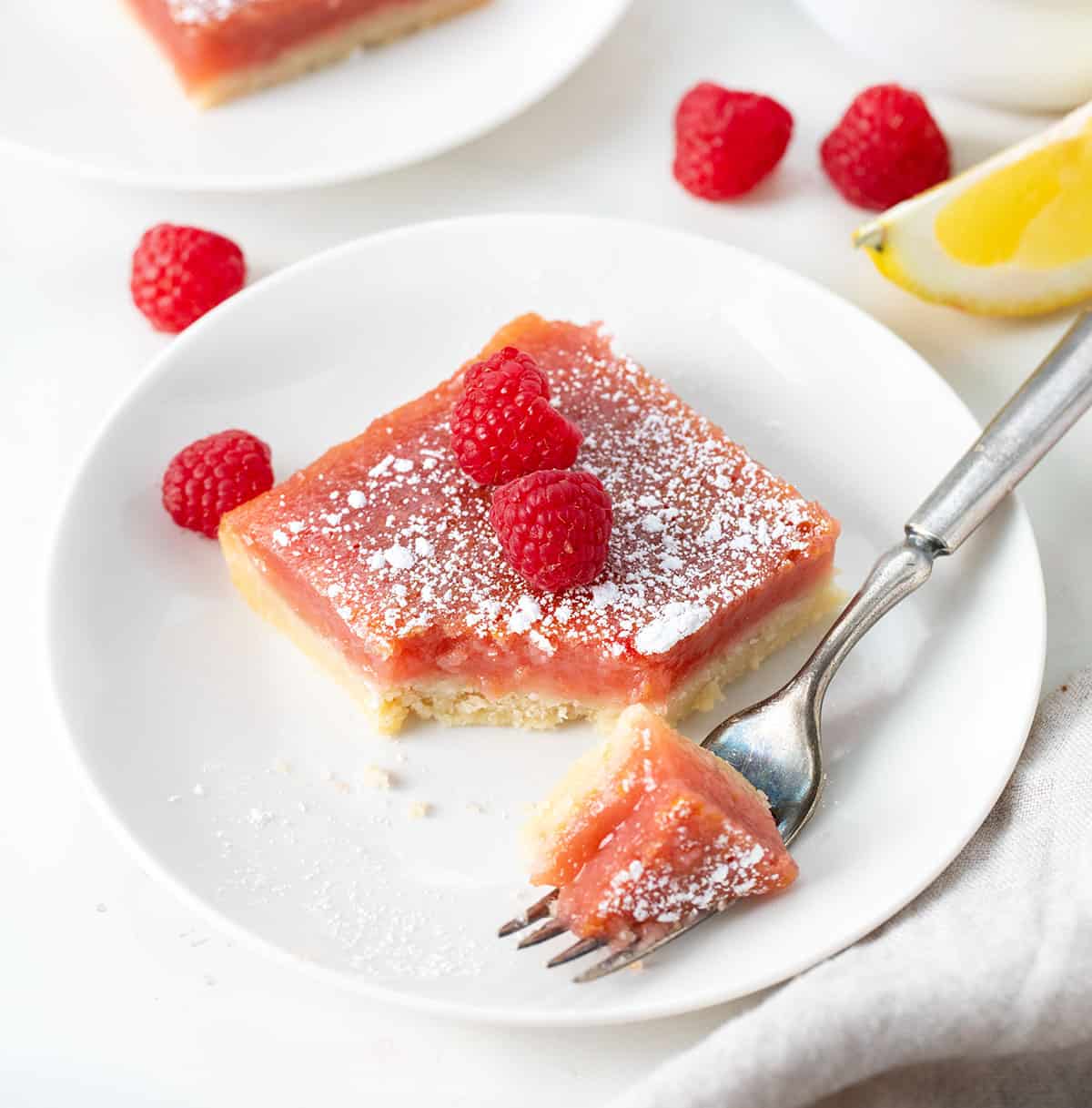 Raspberry Lemon Bar on a white plate with a bite taken out and on the fork.