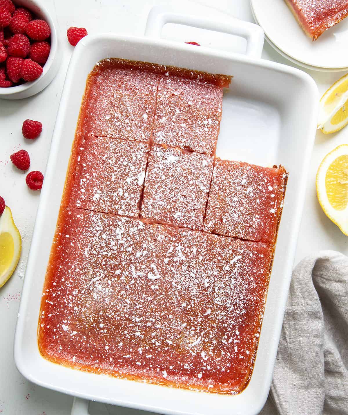 Pan of Raspberry Lemon Bars on a white table with fresh raspberries and lemon wedges from overhead.