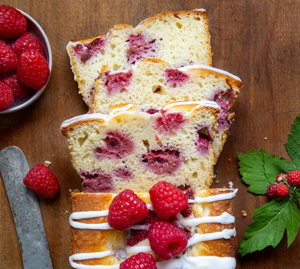 Raspberry Loaf on a wooden table with a few pieces cut and fresh raspberries around.