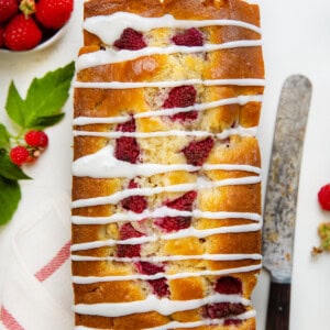 Whole Raspberry Loaf on a white table that is covered in glaze and fresh raspberries.