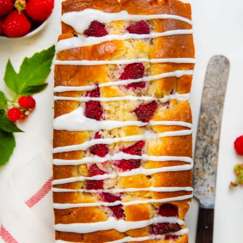 Whole Raspberry Loaf on a white table that is covered in glaze and fresh raspberries.