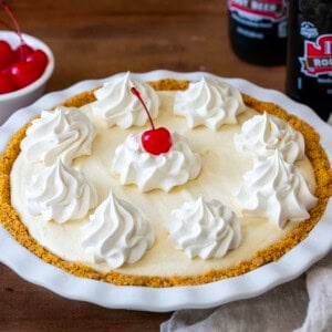 Root Beer Float Pie on a wooden table with root beer bottles and cherries.