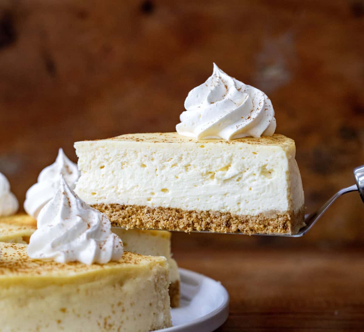 Server picking up a piece of RumChata Cheesecake from a white cake plate.