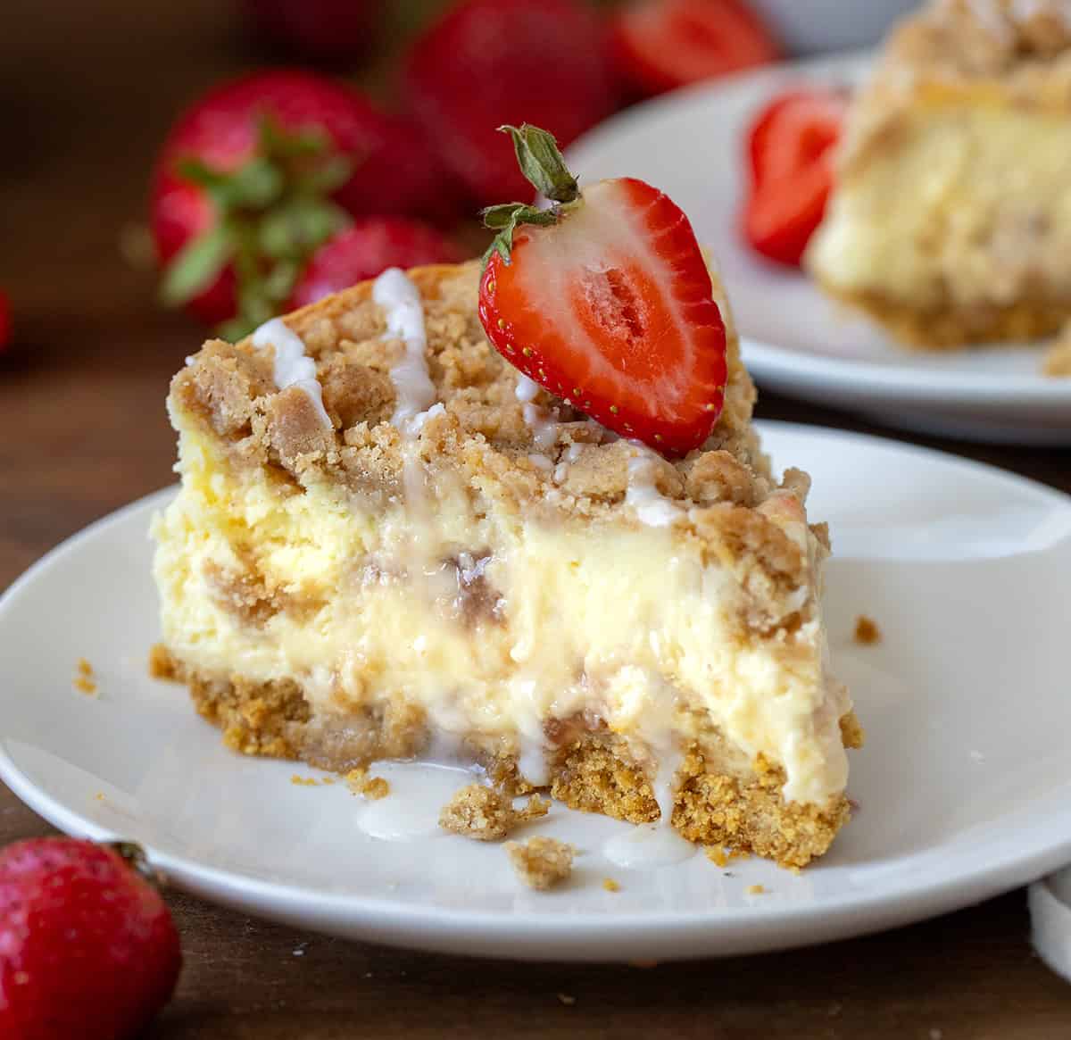 Piece of Strawberry Crumble Cheesecake on a white plate on a wooden table.