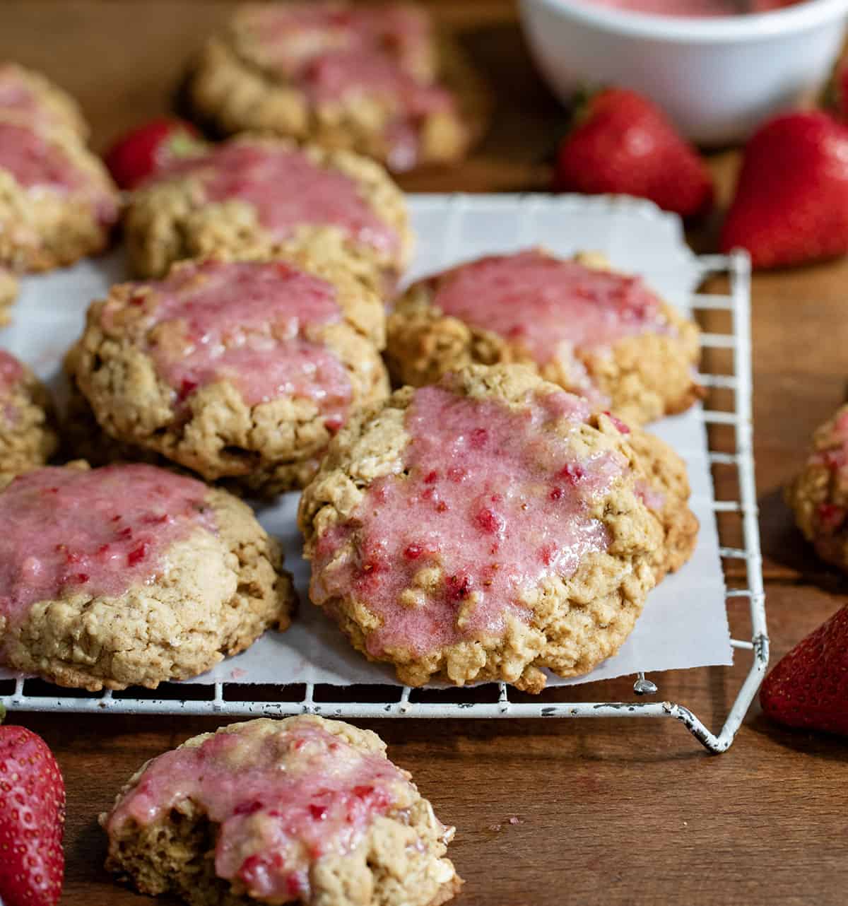 Rack of Strawberry Iced Oatmeal Cookies on a wooden table with fresh strawberries.