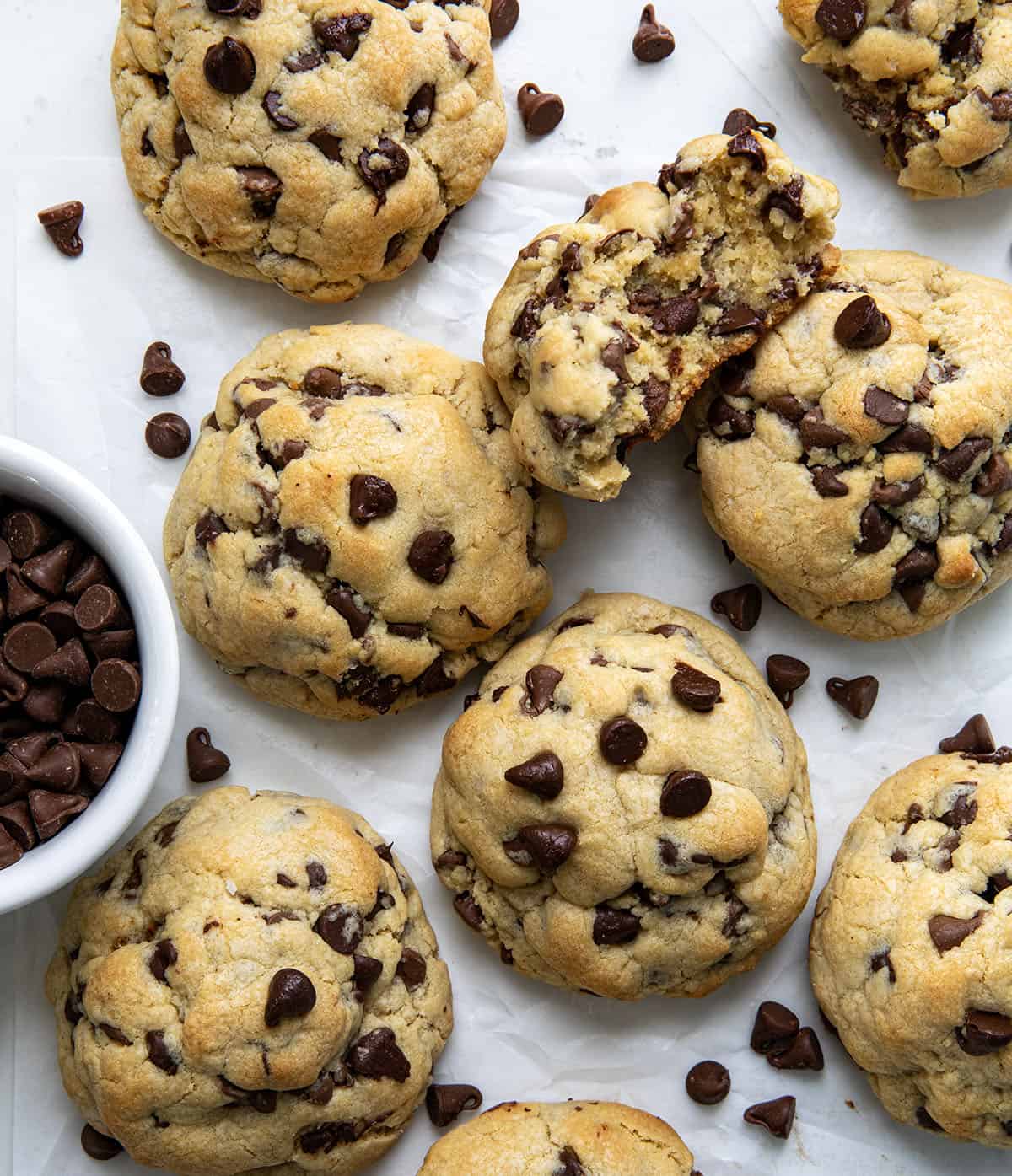 Chocolate Chip Cookies on a white table with one cookie broken in half showing inside texture.