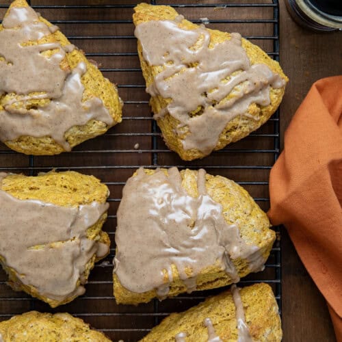 Pumpkin Scones with glaze on a cooling rack with an orange napkin from overhead.