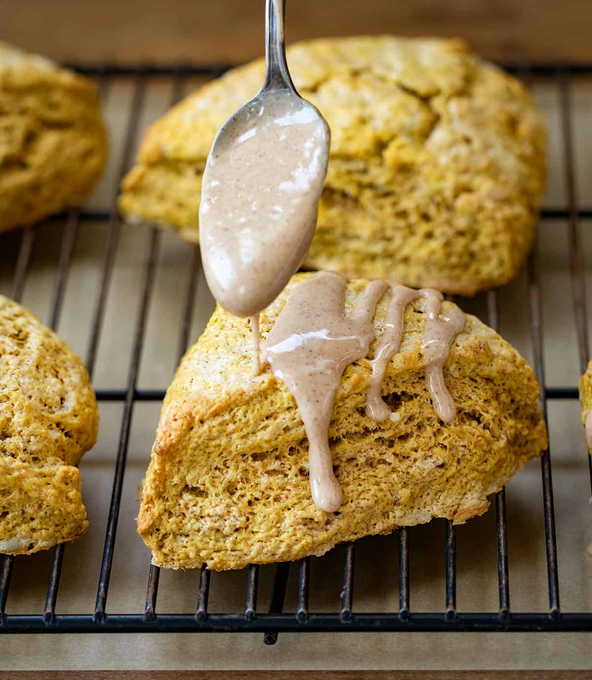 Drizzling glaze over Pumpkin Scones on a wire rack.