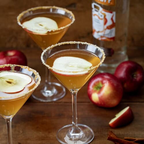 Salted Caramel Apple Martini glasses on a wooden table with fresh apples.