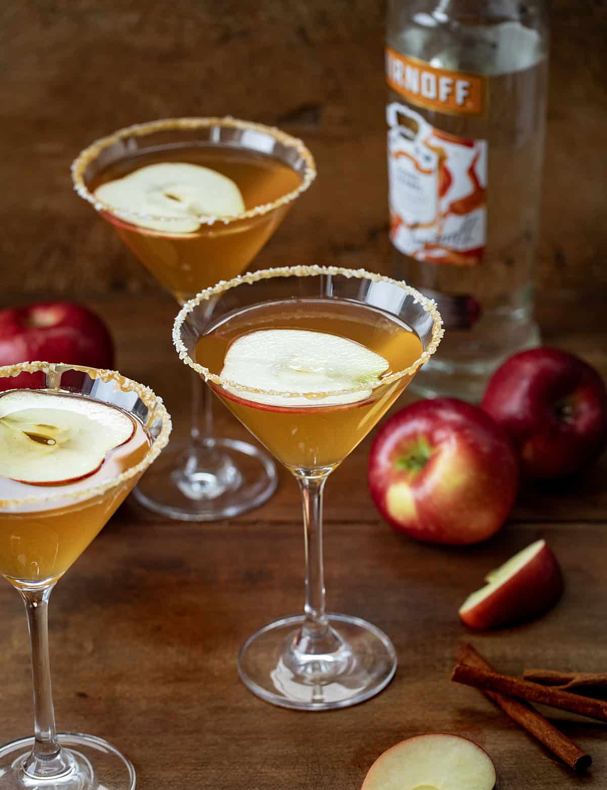 Salted Caramel Apple Martini glasses on a wooden table with fresh apples.