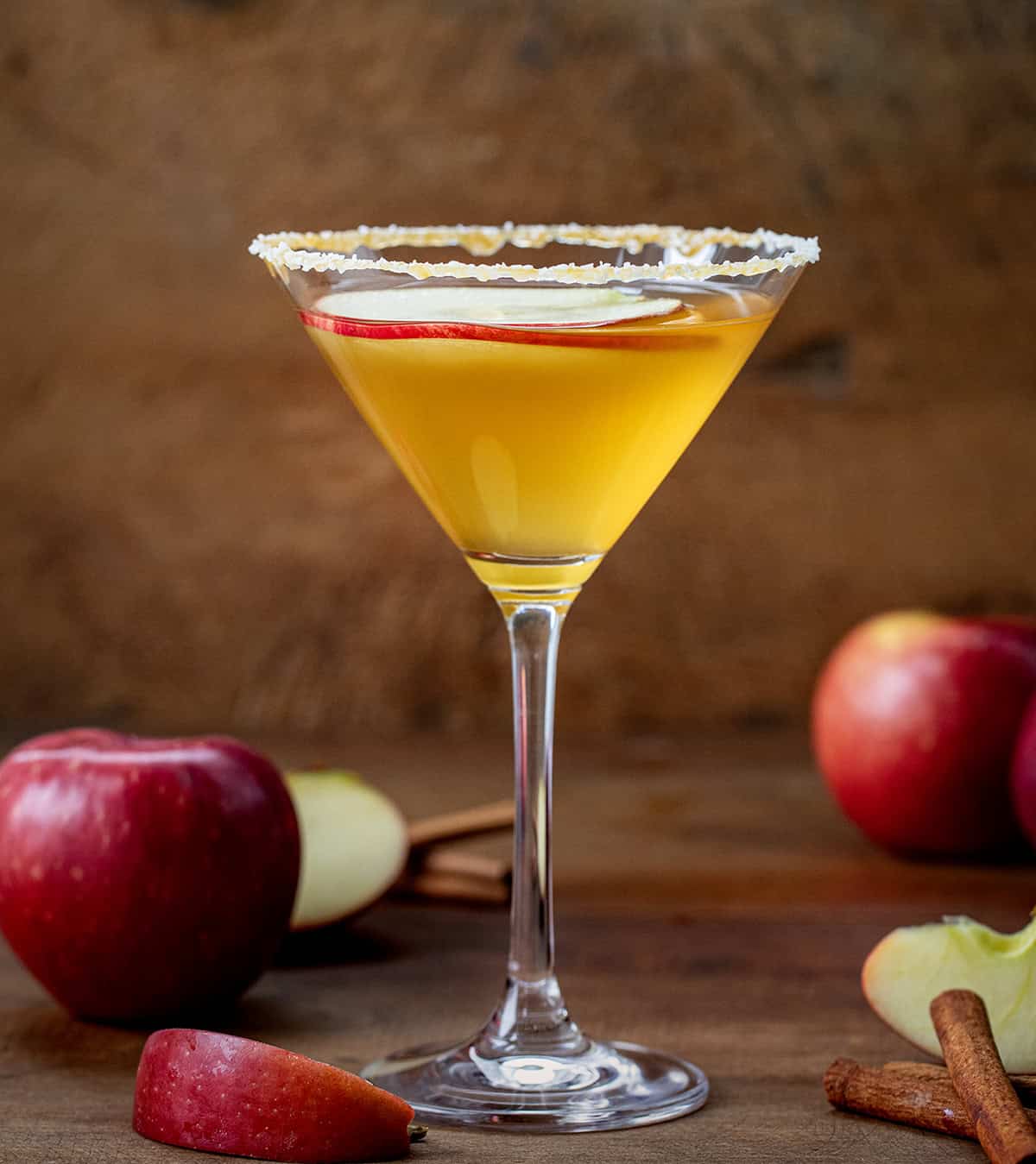 One Salted Caramel Apple Martini on a wooden table surrounded by red apples.