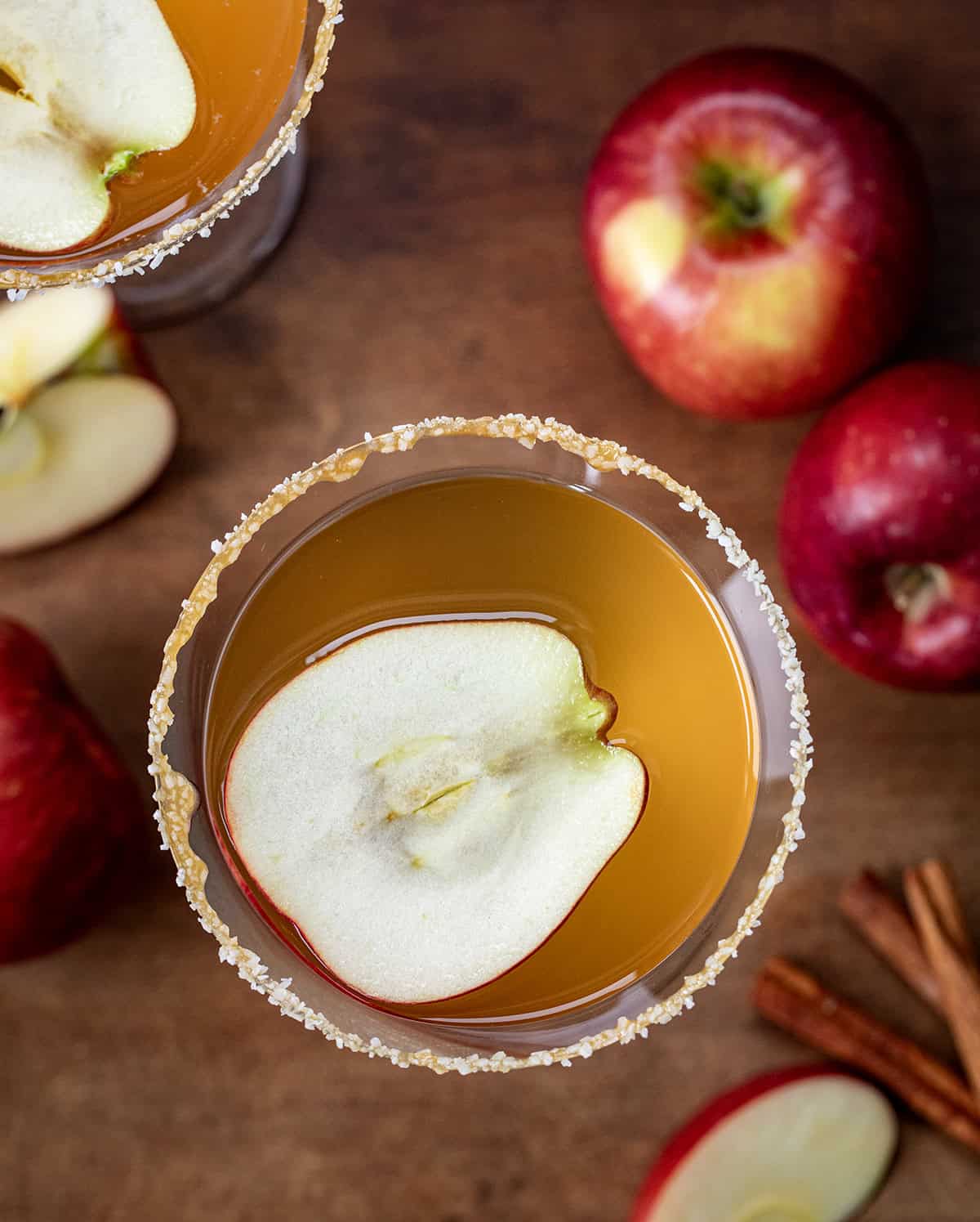 Looking down on Salted Caramel Apple Martini's on a wooden table with fresh apples and cinnamon.