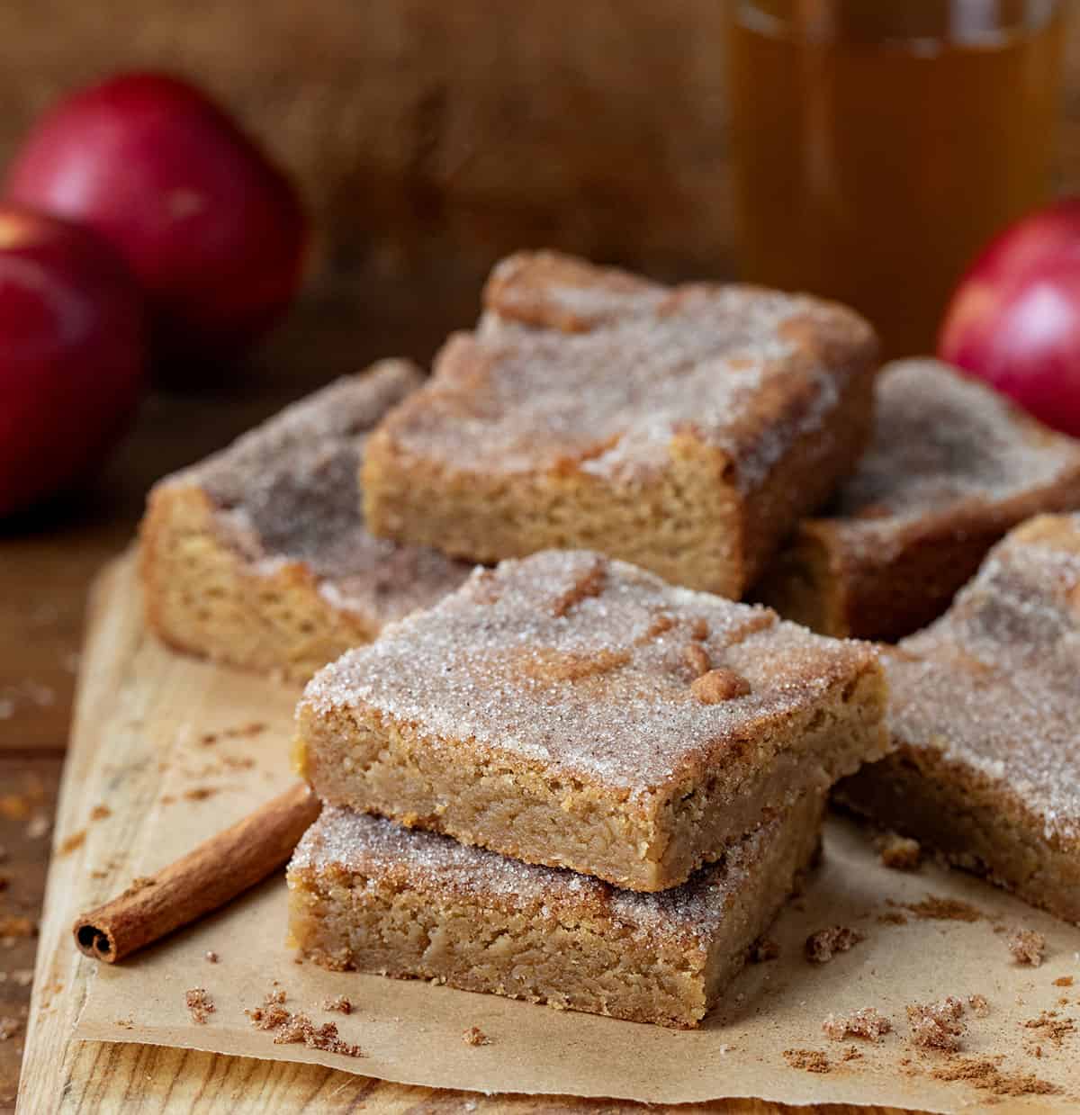 Stacks of Apple Cider Blondies on a cutting board with parchment paper and fresh apples.