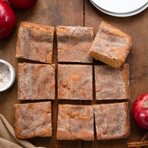 Apple Cider Blondies on a wooden table that are cut into squares with fresh apples and cinnamon sugar.