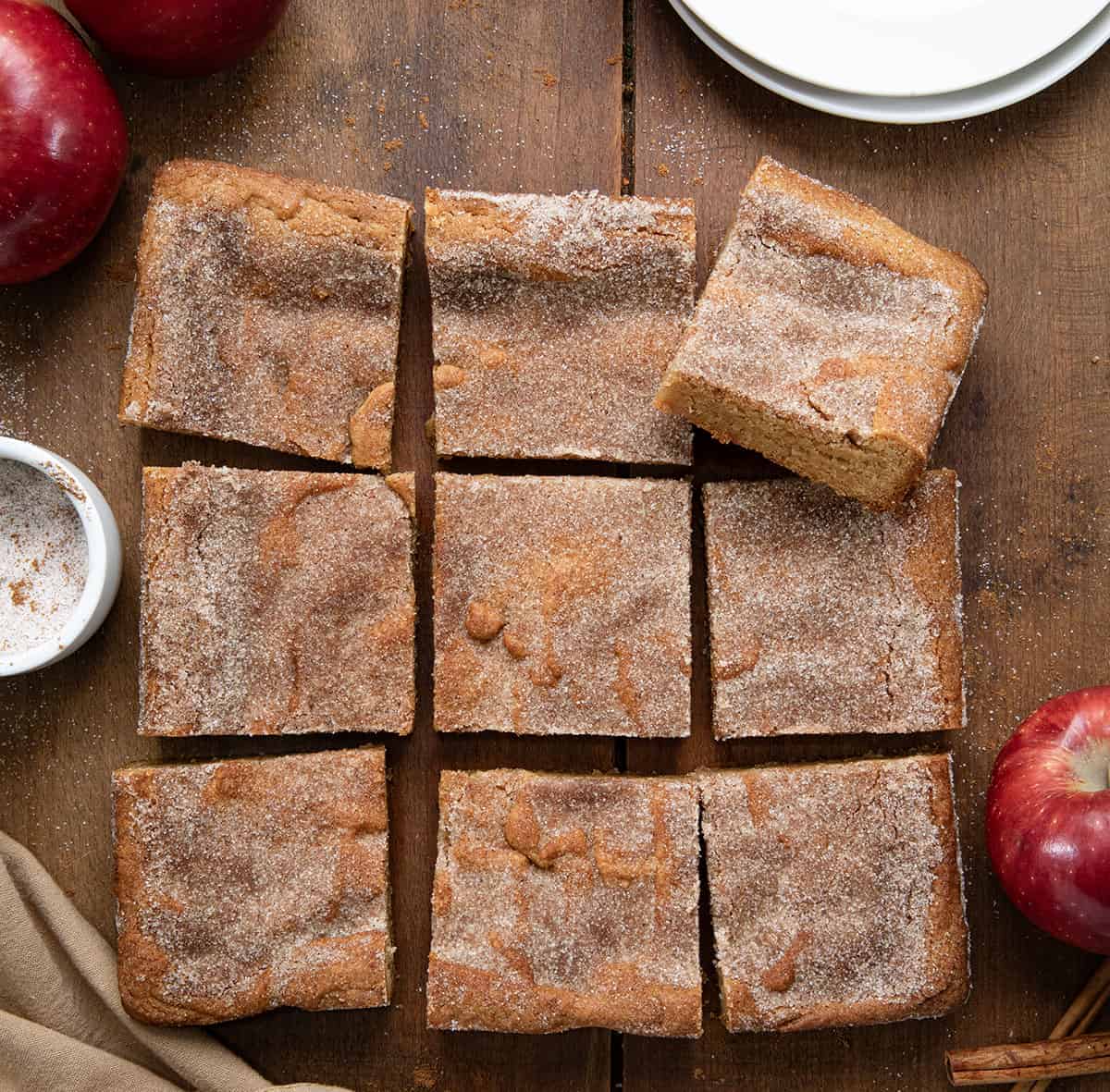 Apple Cider Blondies on a wooden table that are cut into squares with fresh apples and cinnamon sugar.