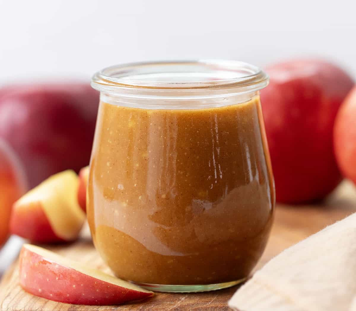 Jar of Apple Cider Caramel Sauce on a wooden table surrounded by apples.