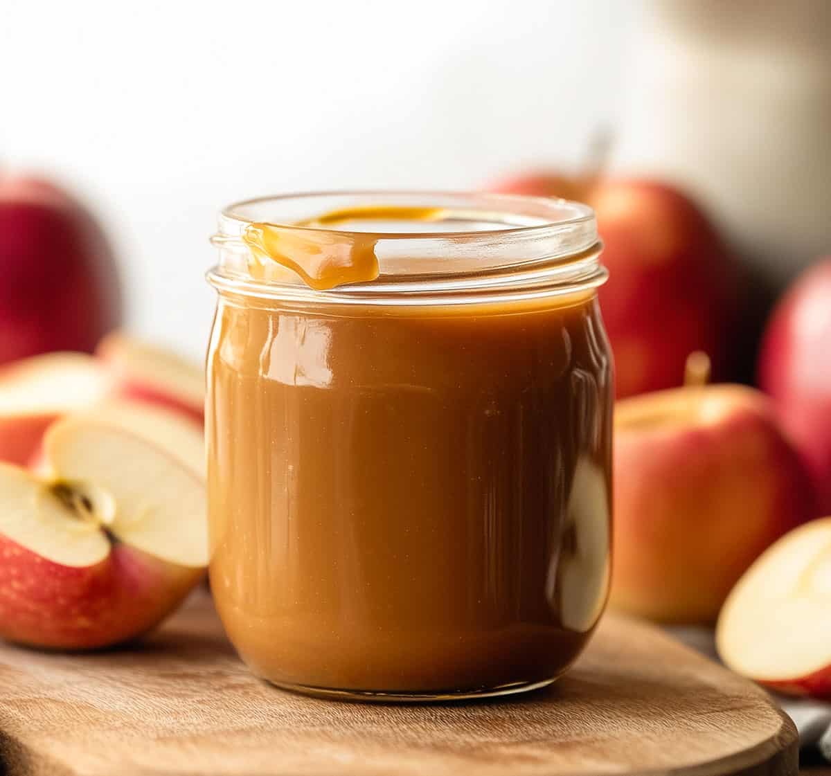 Jar of Apple Cider Caramel Sauce on a wooden table surrounded by apples.
