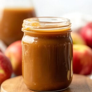 Jar of Apple Cider Caramel Sauce on a wooden table surrounded by apples.