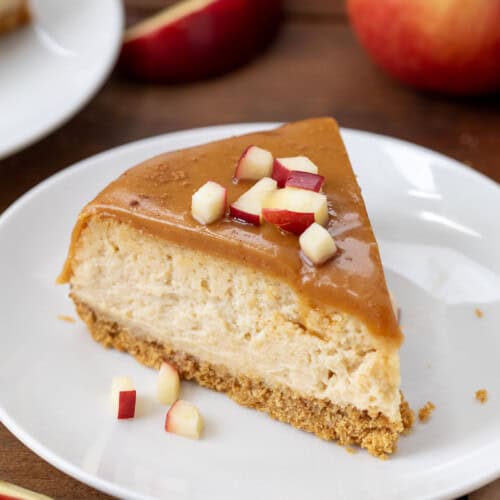 Slice of Apple Cider Cheesecake on a white plate with small apple slices.