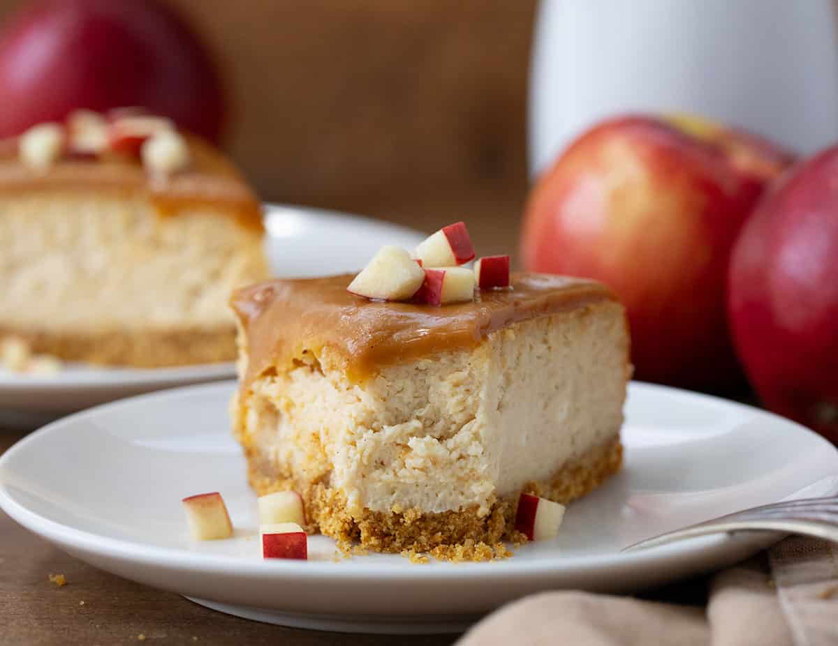 Slice of Apple Cider Cheesecake on a white plate with a bite taken out of it and fork resting on the edge of the plate.