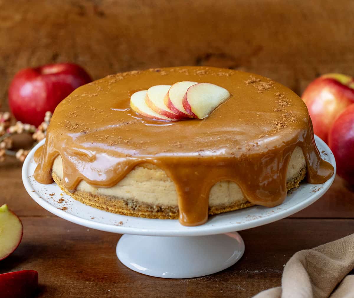 Whole Apple Cider Cheesecake on a wooden table with fresh apples around.