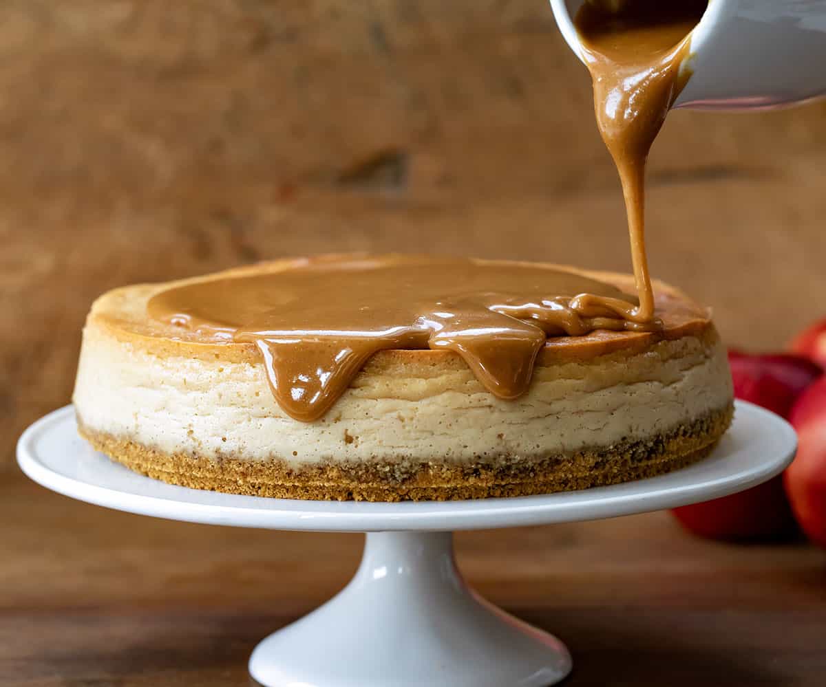 Pouring Apple Cider Caramel over cheesecake on a cake stand.