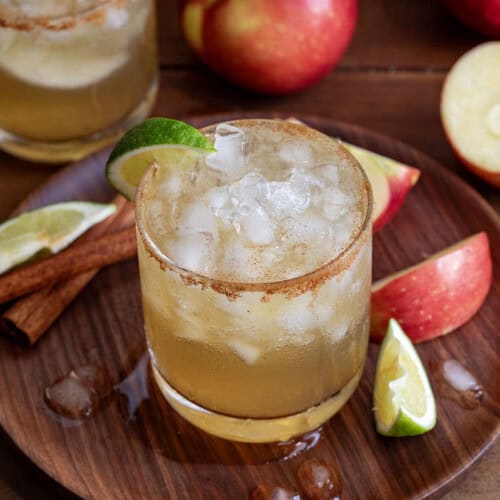 Glasses on Apple Cider Margarita on a wooden table and wooden plate with fresh apple and limes.