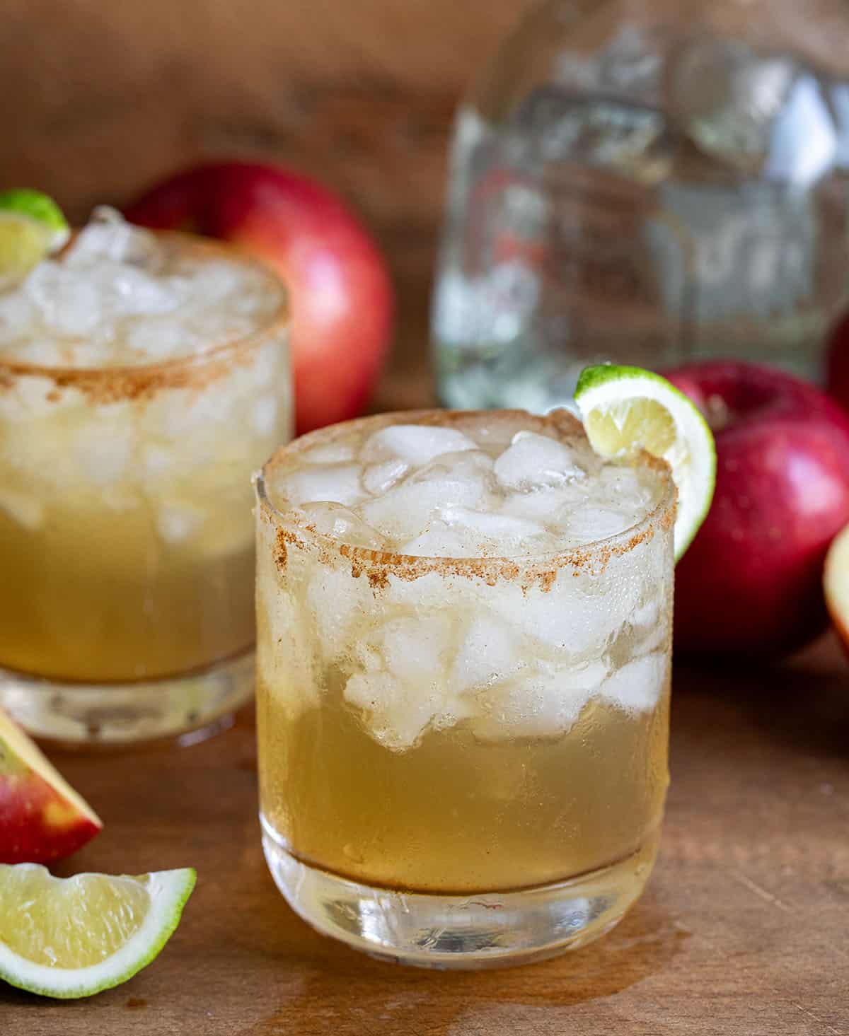 Glasses on Apple Cider Margarita on a wooden table and wooden plate with fresh apple and limes.