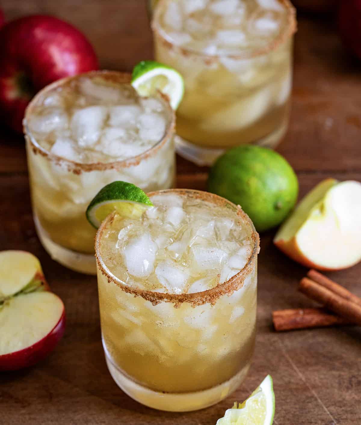 Glasses on Apple Cider Margarita on a wooden table and wooden plate with fresh apple and limes.